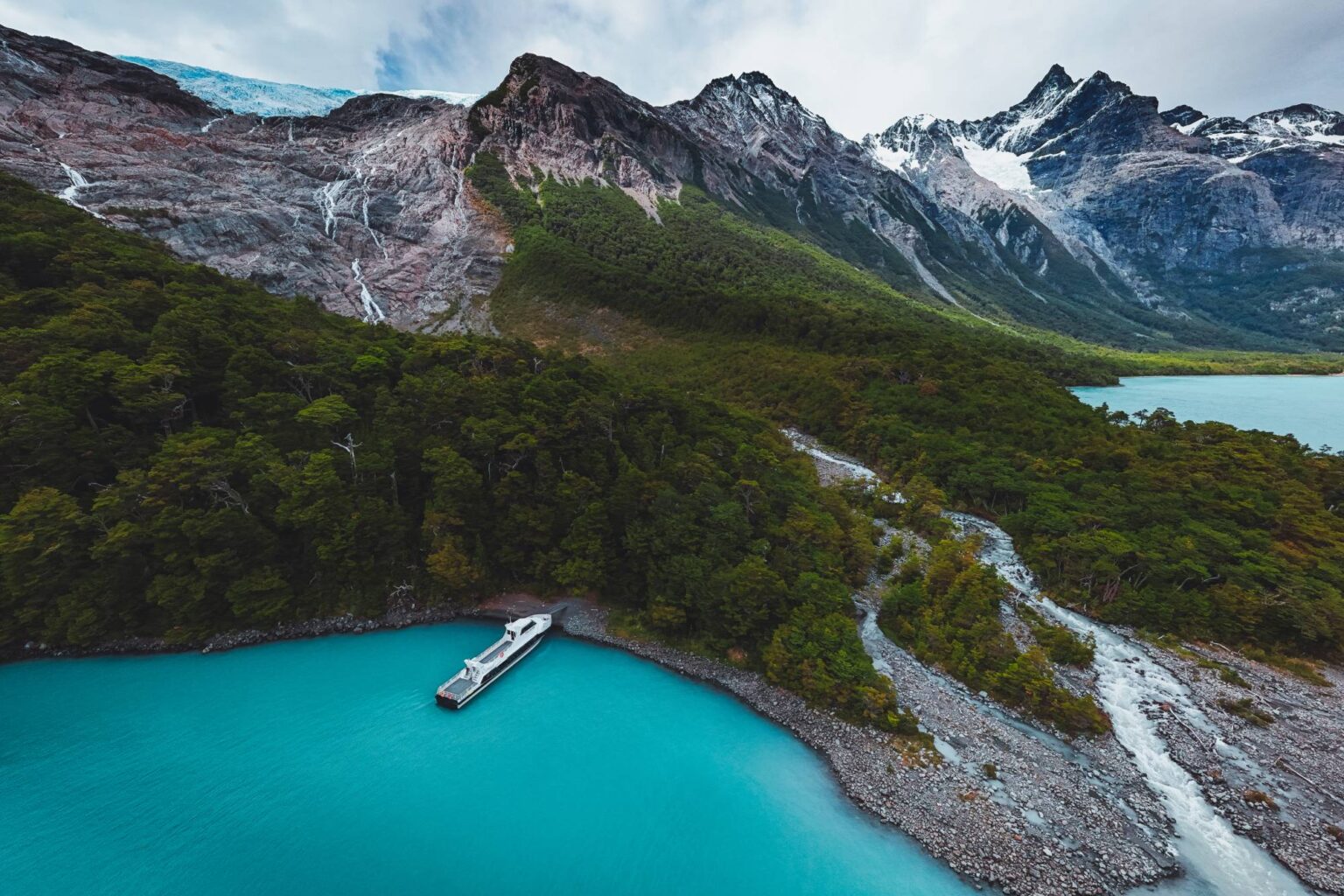 Vista aérea de la embarcación en el Canal Mayo, con el bosque andino y los glaciares colgantes